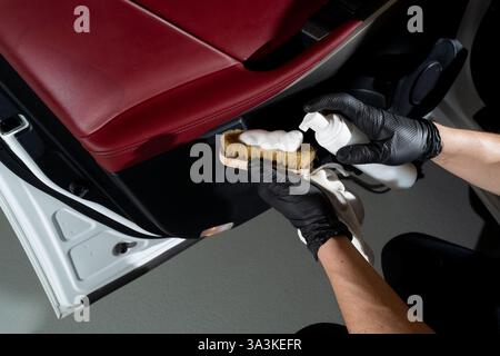 Car detailer cleans the auto door with brush and detergent. Process of removing dust and dirt from the auto door panel Stock Photo