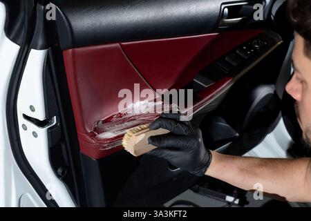 Car detailer cleans the auto door with brush and detergent. Process of removing dust and dirt from the auto door panel Stock Photo