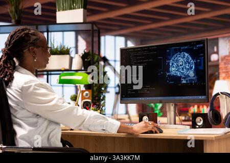 Freelancing computer engineer doing maintenance on artificial intelligence systems, sitting at apartment office desk. African american IT specialist at working from home, doing checkup on AI systems Stock Photo