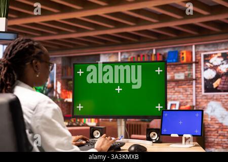 Student at home browsing online on isolated screen computer and tablet, doing homework. African american girl in apartment reading articles on chroma key PC and mockup device for school tasks Stock Photo