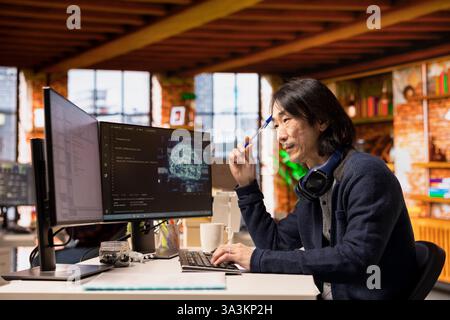 Software developer in small business workspace using computer to oversee artificial intelligence neural networks. Man in tech startup office using AI machine learning systems on PC Stock Photo