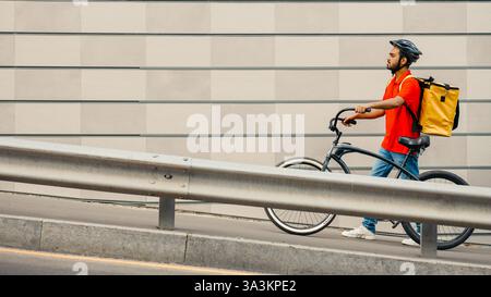 People, delivery and city concept. Courier with helmet and backpack walks along track with bicycle Stock Photo