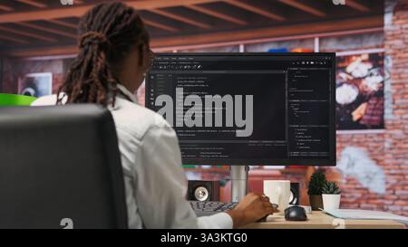 Programmer types code into PC, entering commands, running script. African american IT professional in apartment fixing errors in application, implementing new features, camera B Stock Photo