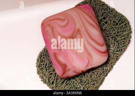 A bar of pink soap on a green soap mat Stock Photo