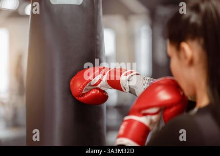 A woman practices boxing techniques on a punching bag in a gym setting Stock Photo