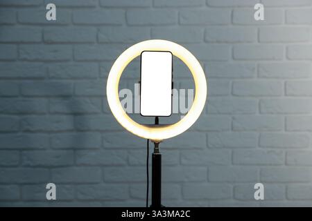 Ring lamp with smartphone against brick wall Stock Photo