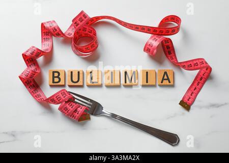 Word Bulimia, fork and measuring tape on white marble table, top view Stock Photo