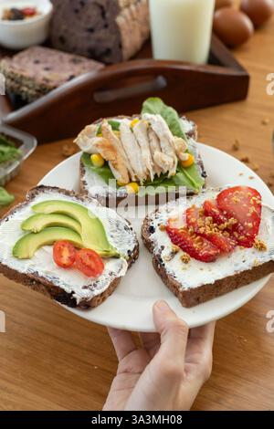 An elegant presentation of three refined toasts, each topped with a smooth layer of cream cheese. One features ripe tomato slices, the second fresh av Stock Photo
