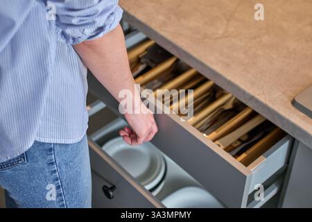 Person opens a kitchen drawer with various utensils in wooden cutlery tray. Woman opening kitchen cabinet. Concept of home organization and functional Stock Photo
