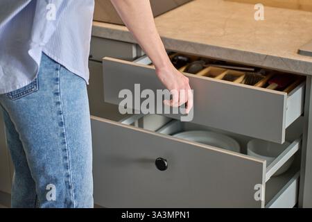 Person opens a kitchen drawer with various utensils in wooden cutlery tray. Woman opening kitchen cabinet. Concept of home organization and functional Stock Photo