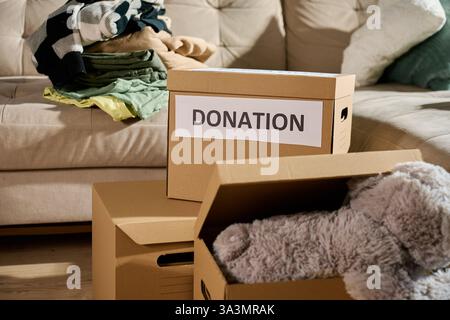 Donation boxes filled with clothes and stuffed toy on couch. Charity and community aid concept Stock Photo