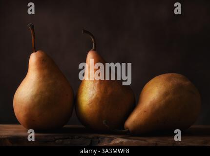Fruit Still Life. Three Bosc Pears on wooden surface with rough edges against a mottled brown background. Stock Photo