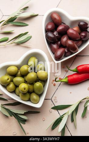 Green and black olives served in heart shaped bowls, decorated with olive tree branches, chili peppers and himalayan salt, creating an elegant and app Stock Photo