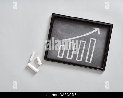 Bar chart drawn in chalk on a blackboard showing growth and improvement with an upward arrow, suggesting positive business trends Stock Photo