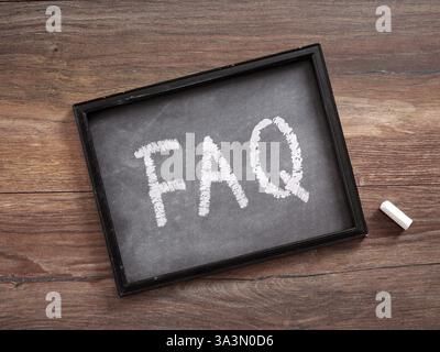 Frequently asked questions written on a small blackboard with piece of chalk resting on wooden table Stock Photo