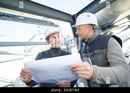 supervisor with workers examining blueprints at table in industry Stock Photo