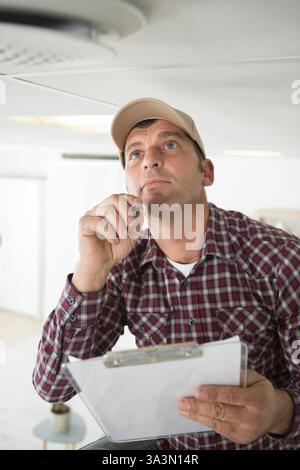 male technician looking at smoke detector and taking notes Stock Photo