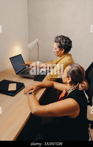 Two mature professionals collaborate on a project, discussing and analyzing data shared on a laptop. Stock Photo