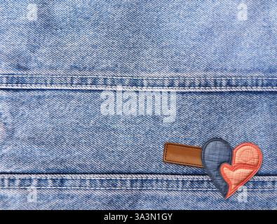 Light blue denim background with felt heart and leather label. Horizontal blue color denim jeans fabric texture with heart-shaped textile patch. Valen Stock Photo