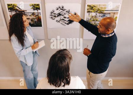 Three professionals discussing and evaluating architectural designs in a collaborative meeting environment. Stock Photo