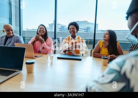 A joyful team of diverse professionals engages in a lively meeting at a modern agency. The atmosphere is cheerful, with laughter and collaboration amo Stock Photo