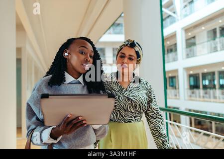 Two multicultural colleagues working together in a modern office environment. They appear focused as they engage in a discussion over a digital tablet Stock Photo