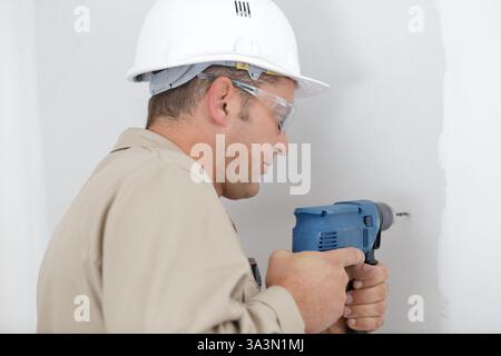 mature tradesman using drill on interior wall Stock Photo