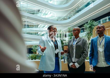 Three confident thought leaders converse in a state-of-the-art office environment, surrounded by contemporary architecture and lush greenery. This sce Stock Photo
