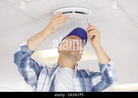 electrician installing smoke detector on ceiling Stock Photo
