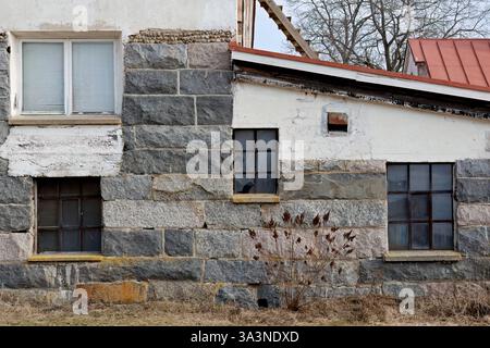 An old stony building with different size windows on the wall Stock Photo