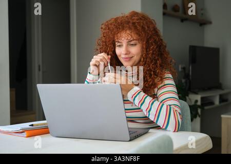 Young woman working from home drinking and looking at laptop Stock Photo