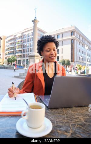 Woman working with laptop and taking notes at outdoors cafe in Madrid Stock Photo
