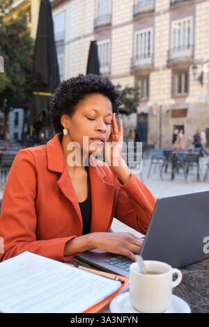 Stressed woman having headache while working on laptop at outdoor cafe Stock Photo