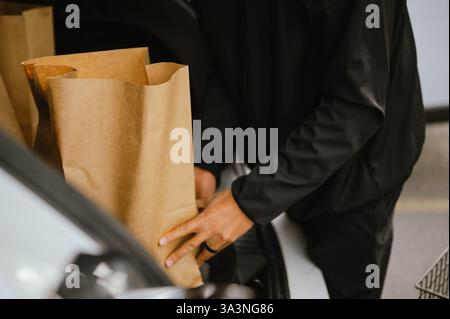 Midsection of young man placing paper grocery bags into trunk of car Stock Photo
