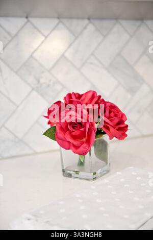 Red roses in a clear glass vase on a white countertop with a til Stock Photo