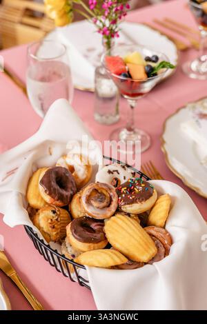 Basket of assorted pastries on a pink table with elegant decor. Stock Photo