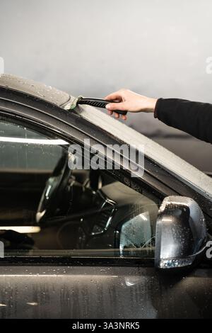 Removing water from windscreen using scraper at car wash service. Process of manual washing car Stock Photo