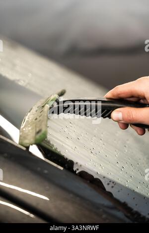 Removing water from windscreen using scraper at car wash service ...