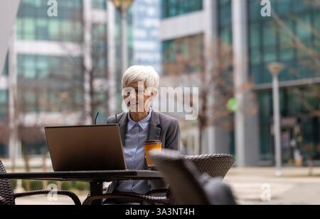 Mature business woman sitting in cafe in urban cityscape and working on laptop Stock Photo