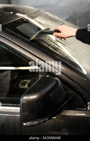 Removing water from windscreen using scraper at car wash service. Process of manual washing car Stock Photo