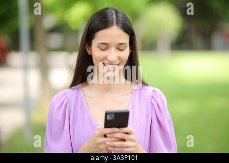 Front view portrait of a happy woman using cell phone walking in a park Stock Photo