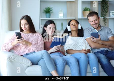 Group of roommates at home enjoying different hobbies sitting on a couch Stock Photo