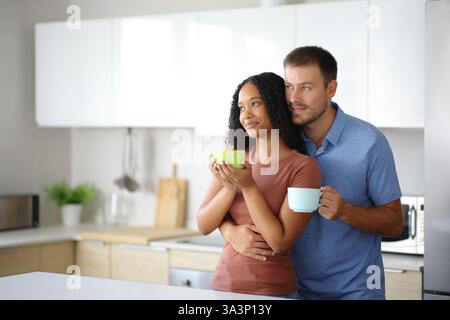 Interracial couple drinking looking away in the kitchen at home Stock Photo