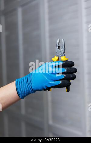 A person in blue safety gloves expertly holds pliers, demonstrating essential tools for various repair tasks Stock Photo