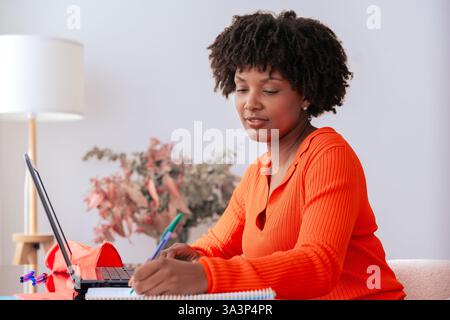 Smiling African American woman studying with laptop and notebook at home Stock Photo