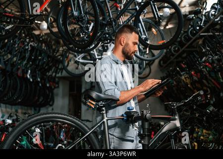 Using digital tablet. Repair man in bicycle shop, working in store. Stock Photo