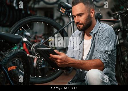 Using digital tablet. Repair man in bicycle shop, working in store. Stock Photo