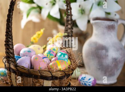 Decorated Easter eggs in a basket with white lilies on rustic wooden background Stock Photo