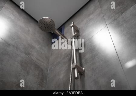 Close-up of a shower head hanging on a rail in a modern bathroom, showcasing sleek design and functionality within a clean and contemporary setting Stock Photo
