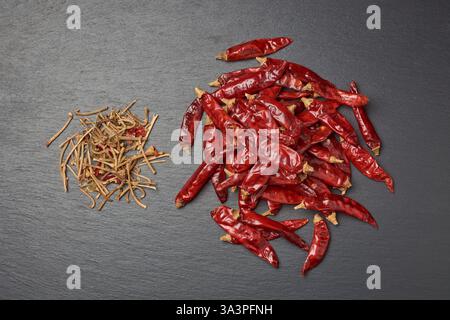 pile of dried chili peppers with stem cut off on black textured surface background, preparation step for making chili powder or flakes, top view Stock Photo